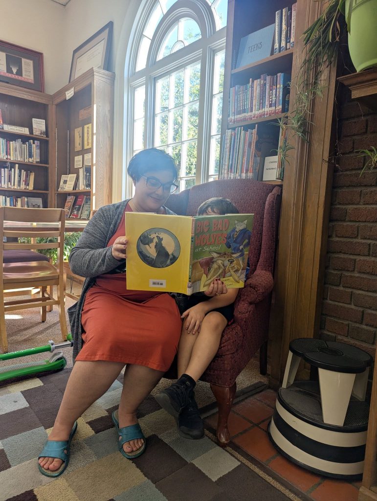 Photo of woman and child reading book in stuffed chair.
