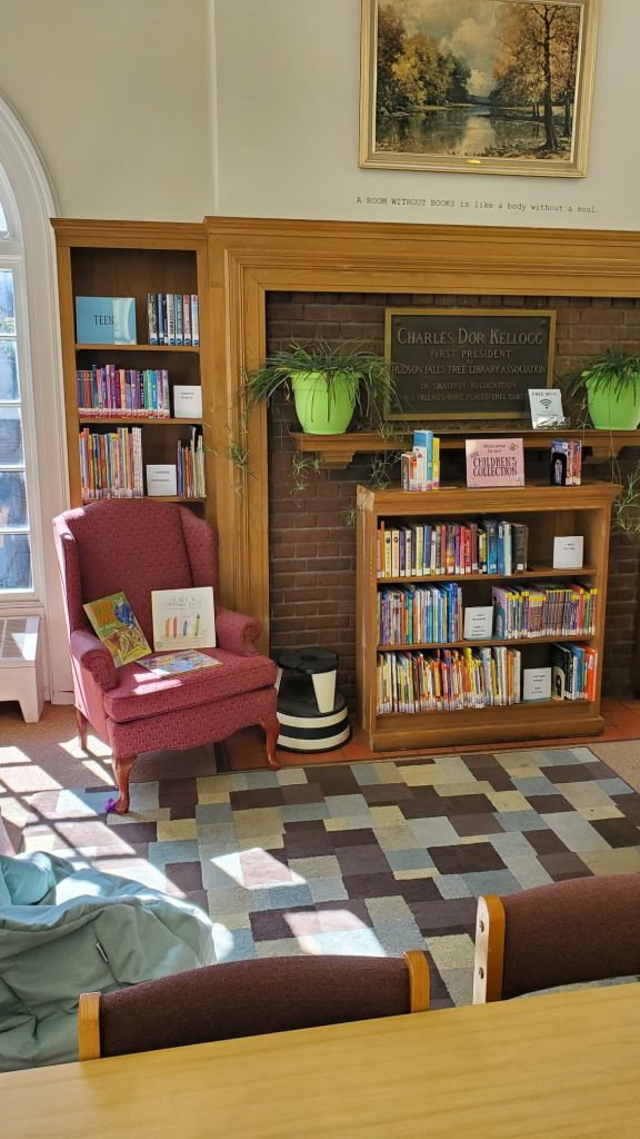 Photo of pop-up children's area upstairs: stuffed chair, rug, beanbag, and kids books on shelf in front of the fireplace.