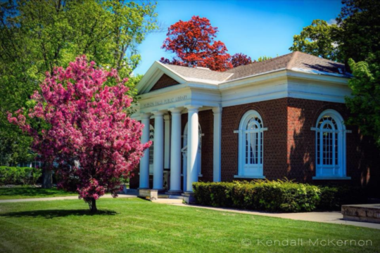 Brick building with white columns surrounded by grass and flowering trees 
