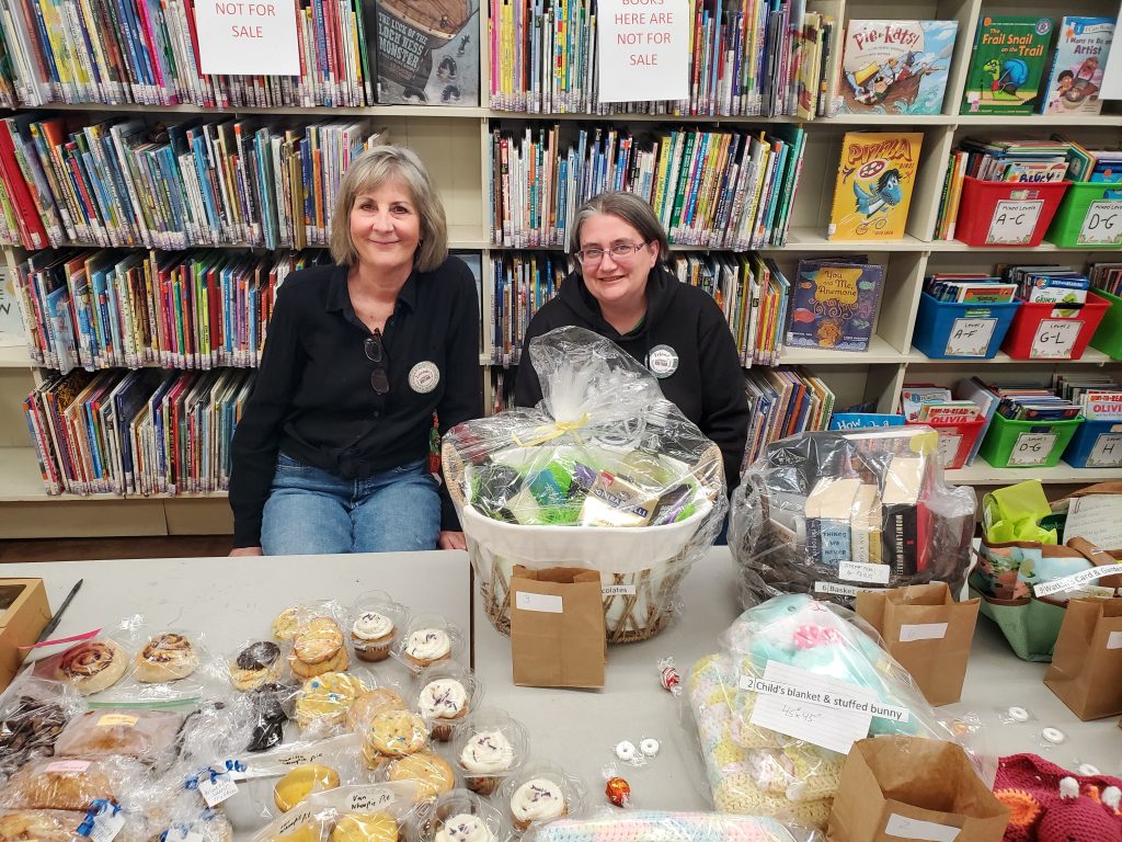 Photograph of two volunteers selling raffle baskets and baked goods