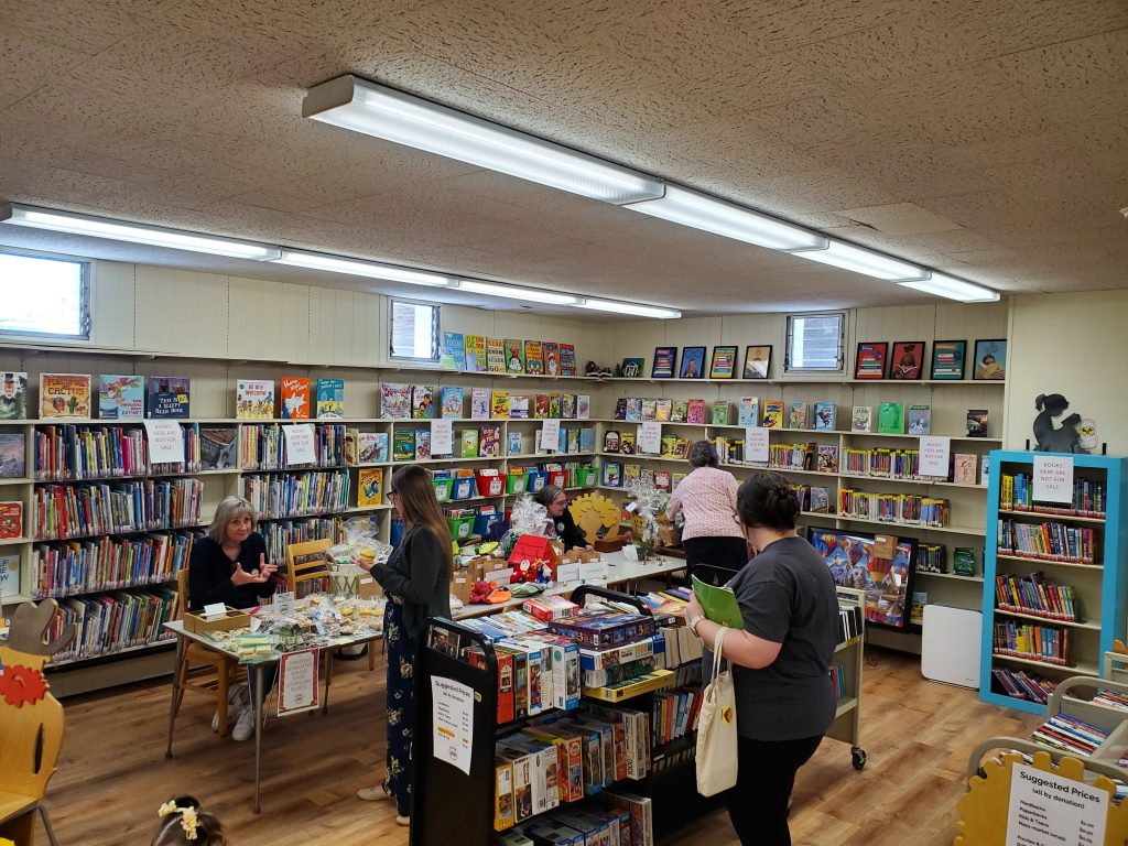 Photograph of people shopping at book carts and bake sale downstairs in a library